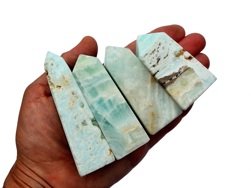 Four small blue caribbean calcite obelisks on hand with white background