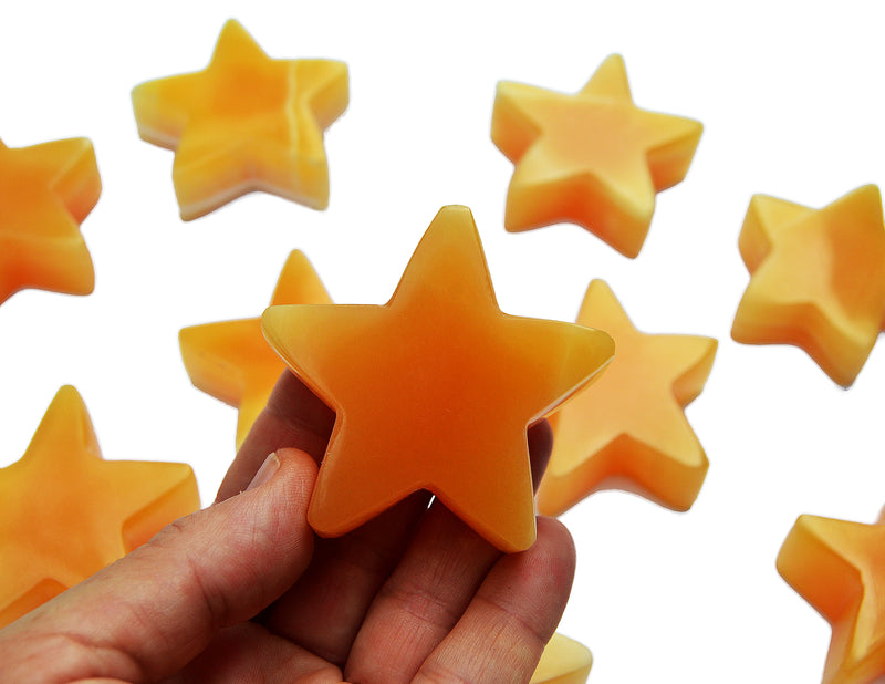 One orange calcite star carving crystal 55mm on hand with background with some stones on white