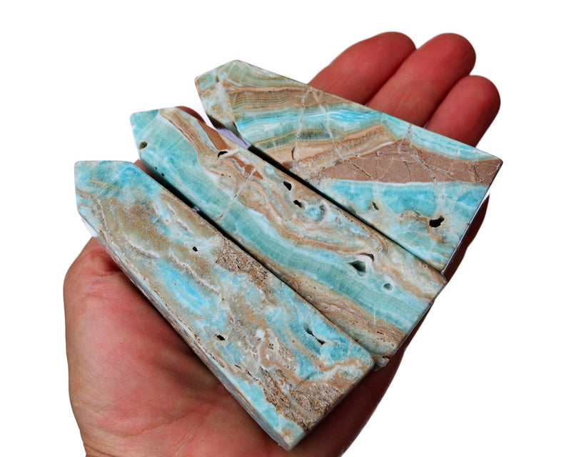 Three blue aragonite obelisk crystals on hand with white background