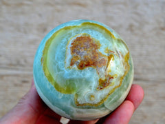 Large green pistachio calcite sphere crystal 80mm on hand with wood background