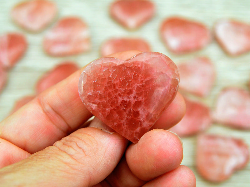 One rose calcite hart stone 35mm on hand with background with some crystals on wood table