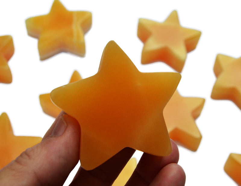 One orange calcite star carving mineral 60mm on hand with background with some stones on white