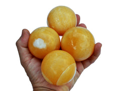 Four orange calcite spheres 55mm-65mm on hand with white background