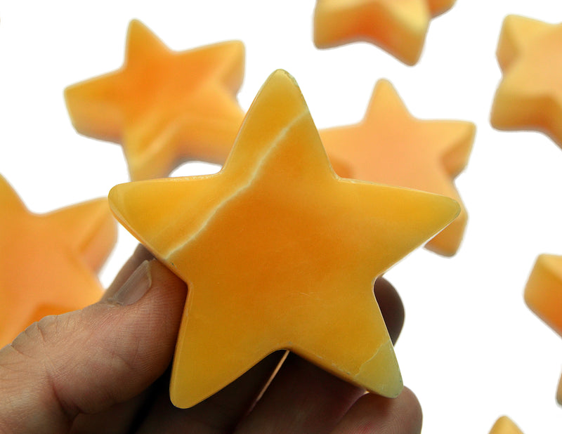 One orange calcite star carving crystal 60mm on hand with background with some stones on white