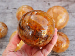 One golden healer quartz sphere 70mm on hand with background with some hematoid balls on wood table