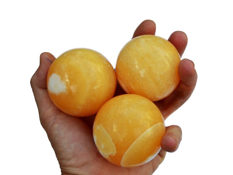 Three orange calcite spheres 55mm-65mm on hand with white background