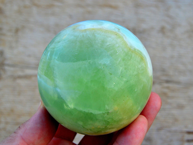 Large green pistachio calcite sphere 75mm on hand with wood background