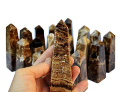 One banded chocolate calcite crystal obelisk on hand with background with several crystals on white