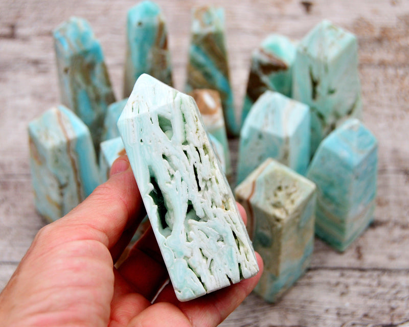 One druzy blue aragonite tower on hand with background with several crystals on wood table