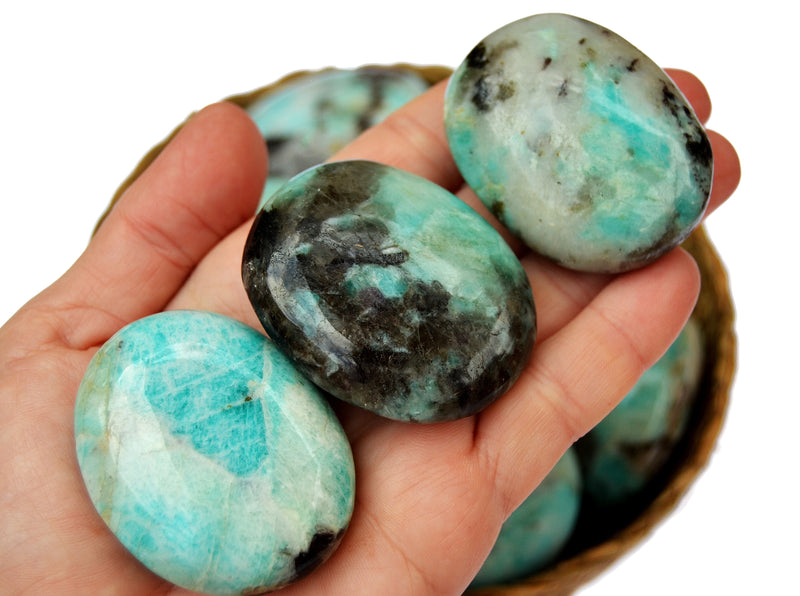 Three amazonite palm stones 60mm-40mm on hand with background with some stones inside a basket