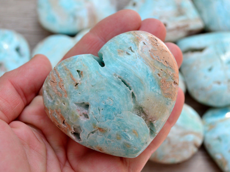One druzy blue aragonite heart crystal 50mm on hand with background with some stones on wood table