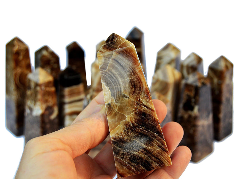 One chocolate calcite crystal obelisk on hand with background with several crystals on white
