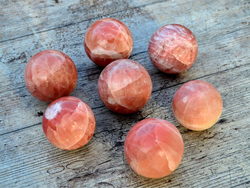 Several rose calcite sphere crystals 55mm-60mm on wood table