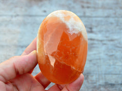 One large honey calcite palm stone 70mm on hand with background with some stones on wood table
