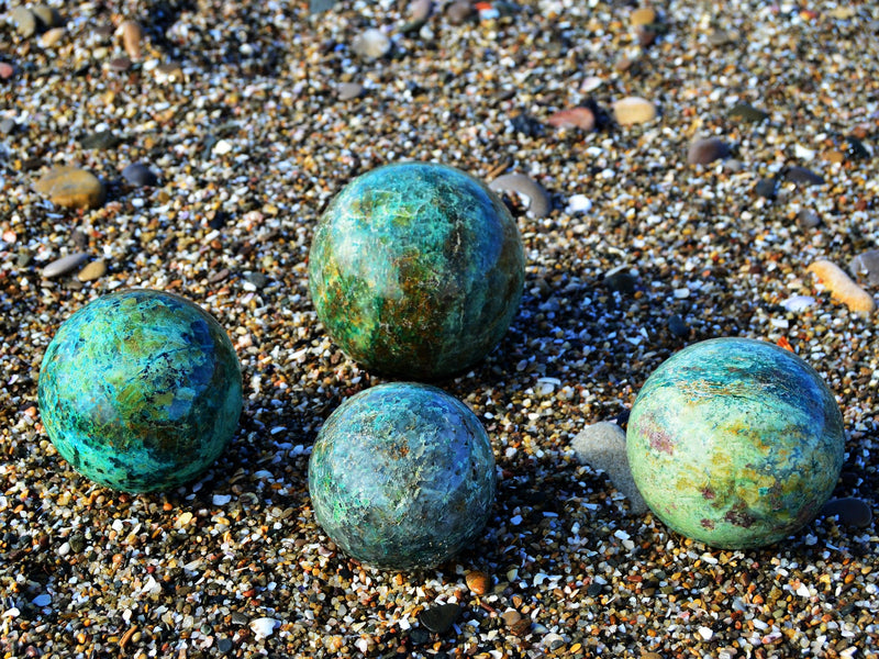 Four green chrysocolla sphere crystals 65mm-100mm on sand background
