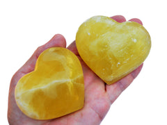 Two large lemon calcite heart crystals 75mm on hand with white background