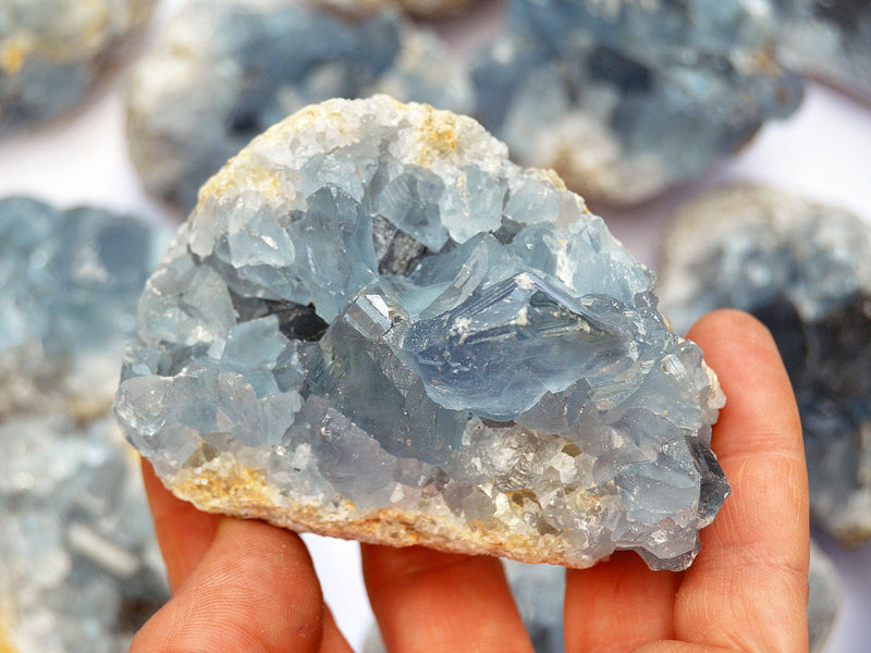 One blue celestite cluster on hand with background with some crystals