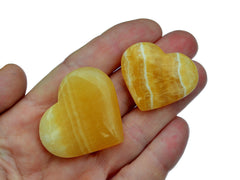 Two orange calcite heart crystals 30mm-40mm on hand with white background