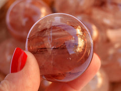 One fire quartz crystal sphere 40mm on hand with background with several spheres