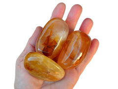 Three big golden healer quartz tumbled stones on hand with white background