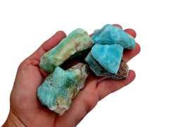Four small blue aragonite raw crystals on hand with white background