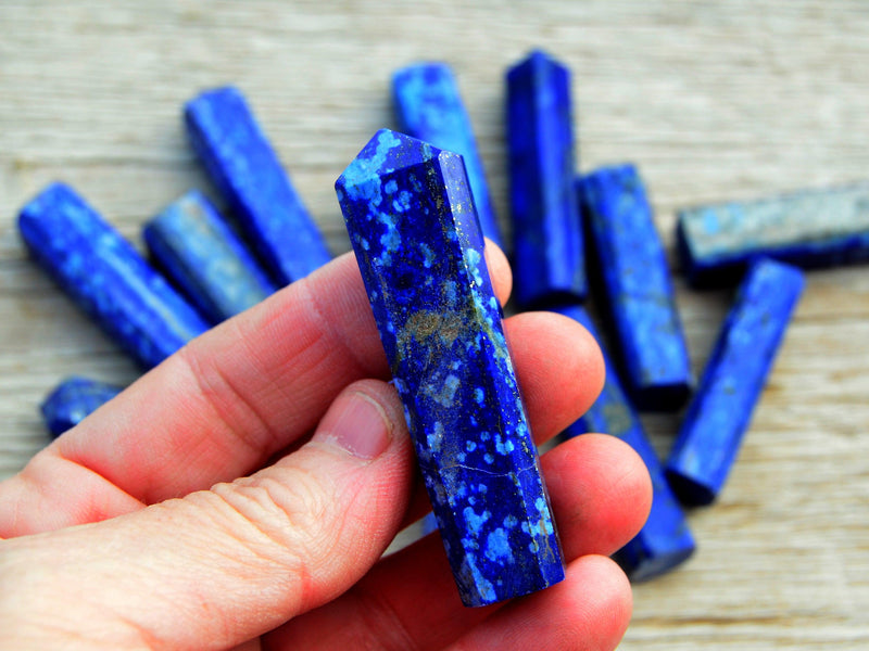 One small lapis lazuli tower point 55mm on hand with background with some crystals on wood table
