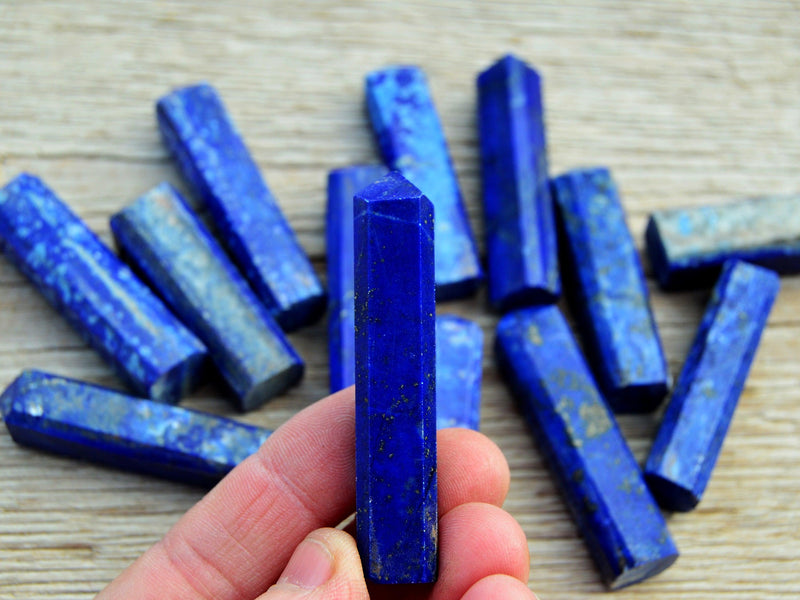 One lapis lazuli crystal point 60mm on hand with background with some crystals on wood table