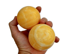 Two orange calcite spheres 55mm-65mm on hand with white background