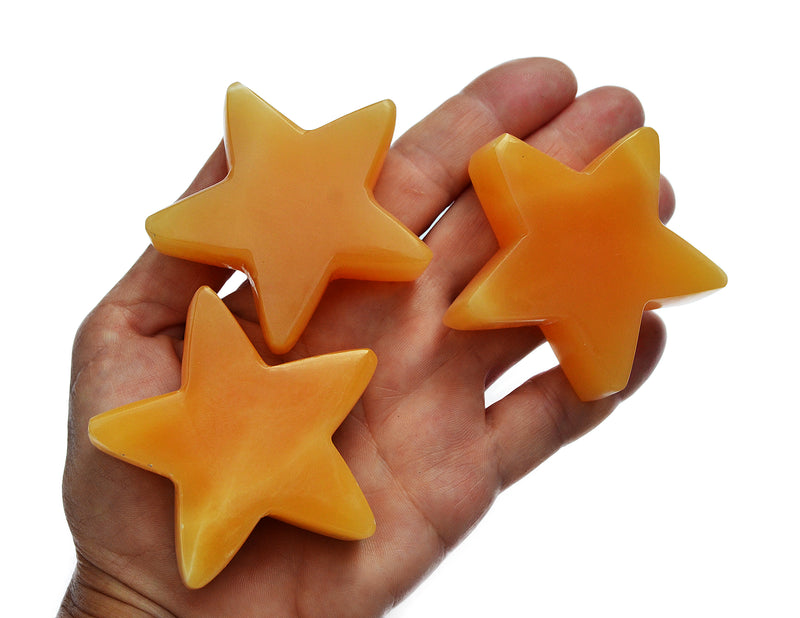 Three orange calcite star carving crystals 55mm-60mm on hand with white background