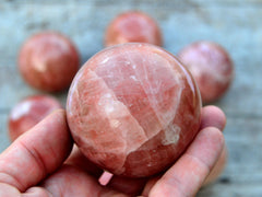 One rose calcite sphere stone 60mm on hand with white background with some balls on wood table