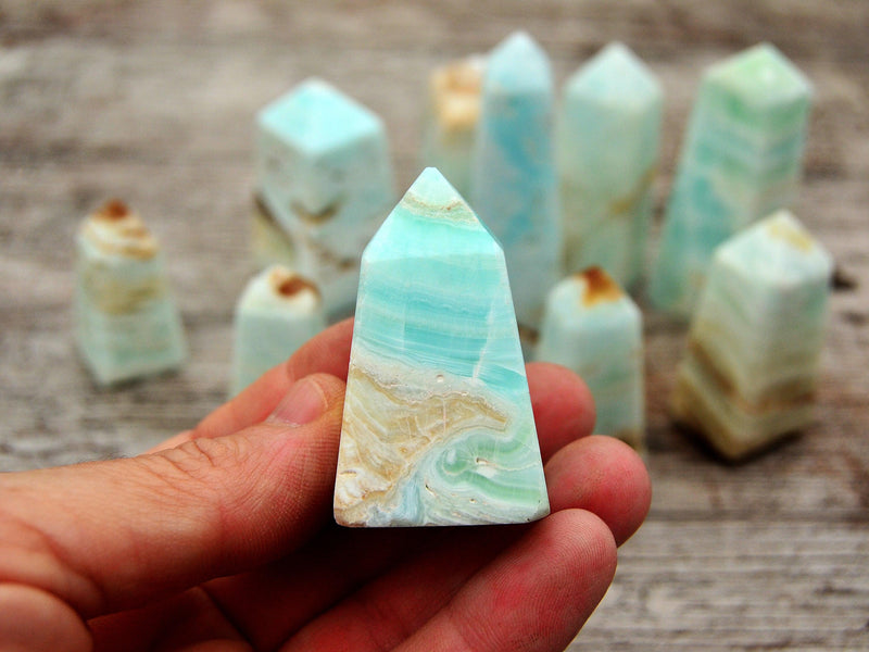 One small caribbean blue calcite crystal tower on hand with background with some crystals on wood table