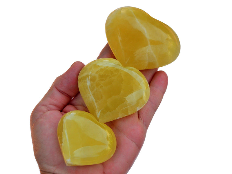 Four lemon calcite heart minerals 50mm-75mm on hand with white background