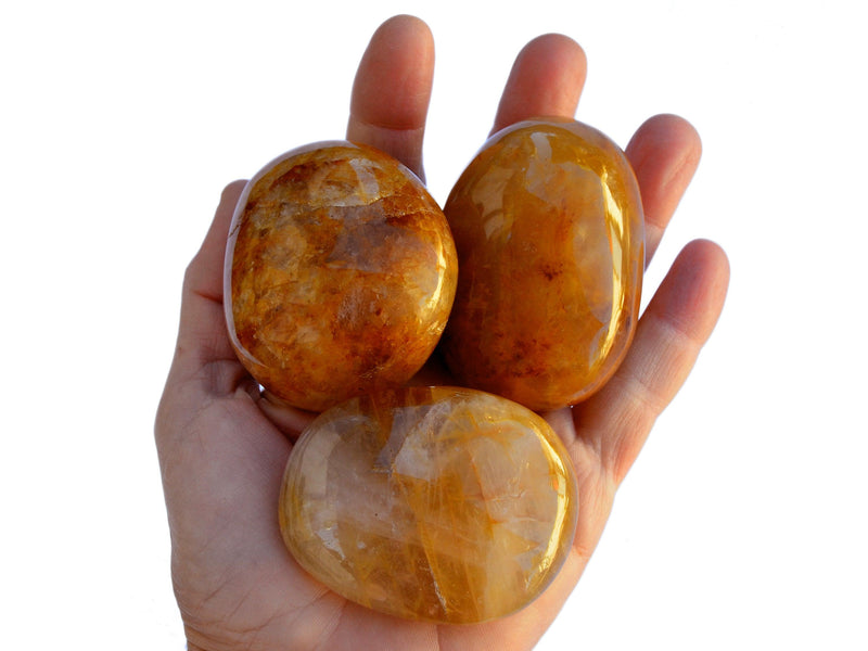 Three large golden healer quartz tumbled crystals on hand with white background
