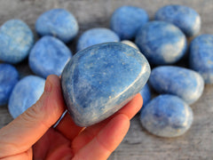 One large blue calcite tumbled crystal on hand with background with some minerals on wood table