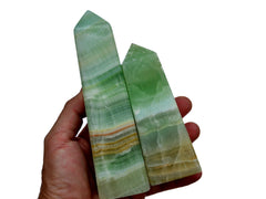 Two large green pistachio calcite crystal obelisks 130mm-145mm on hand with white background