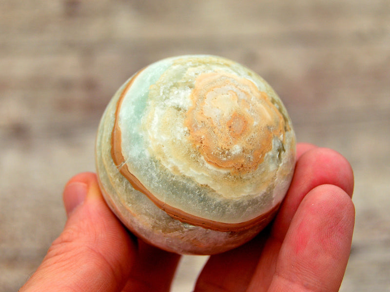 One caribbean calcite sphere crystal 55mm on hand with wood background