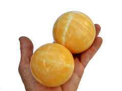 Two orange calcite balls 55mm-65mm on hand with white background