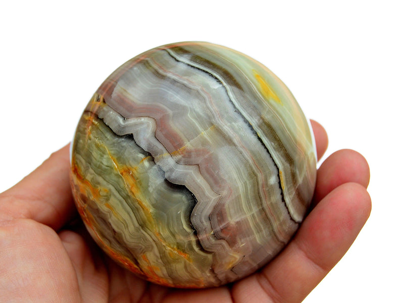 One large pink banded onyx sphere stone 95mm on hand with white background