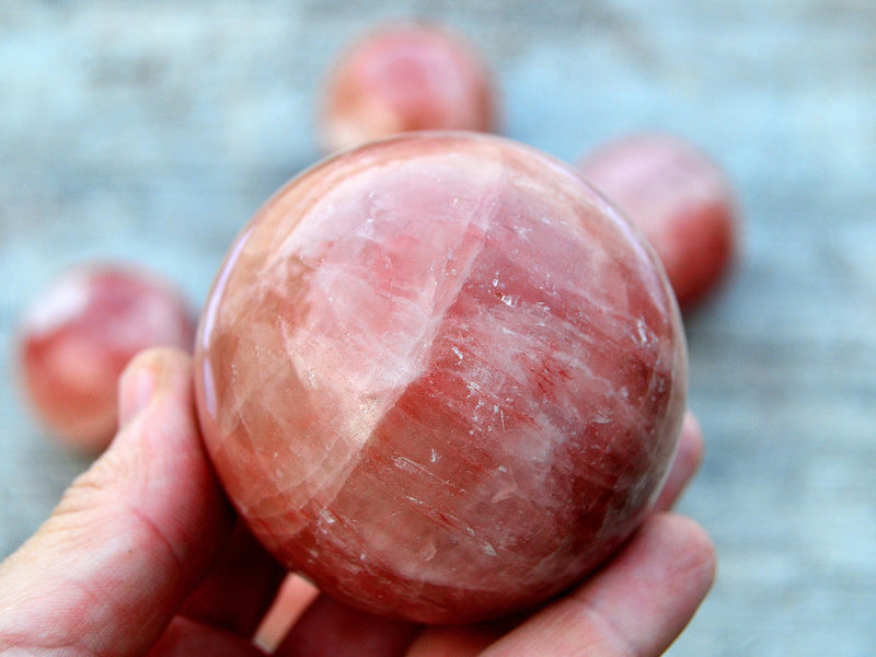 One rose calcite sphere stone 50mm on hand with white background with some balls on wood table