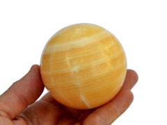 One orange calcite sphere 55mm on hand with white background