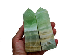 Two chuny banded green pistachio calcite crystal obelisks on hand with white background