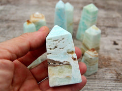 One small druzy caribbean blue calcite crystal tower on hand with background with some crystals on wood table