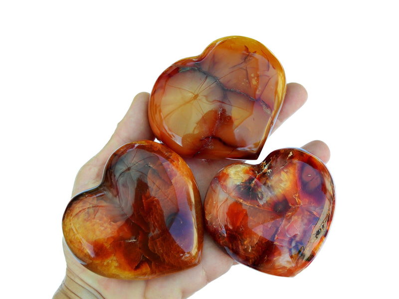 Three large carnelian carved stones on hand with white background