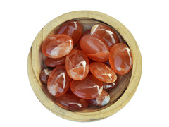 Several honey calcite palm stones inside a wood bowl on white background
