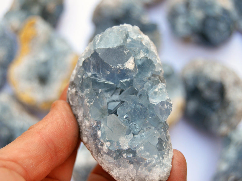 One bluce celestite cluster 60mm on hand with background with some crystals on white