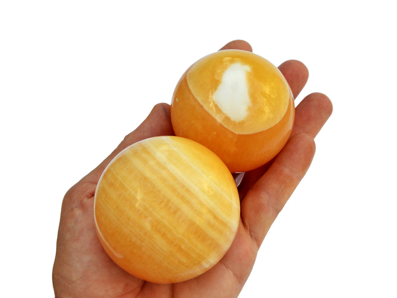 Two orange calcite spheres 55mm-65mm on hand with white background