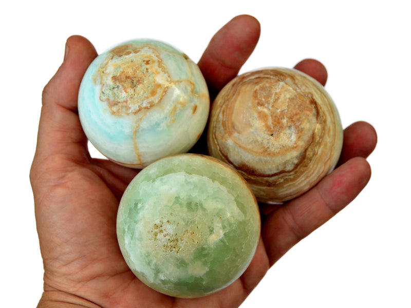 Three caribbean blue green calcite crystal spheres 50mm-60mm on hand with white background