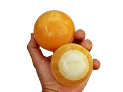 Two orange calcite crystal spheres 75mm on hand with white background