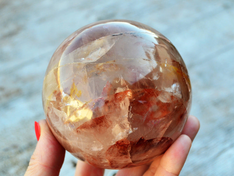 One big fire quartz crystal sphere 90mm on hand with wood background