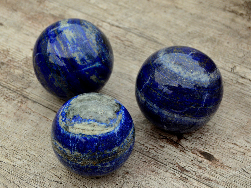 Three blue lapis lazuli sphere crystals 75mm on wood table